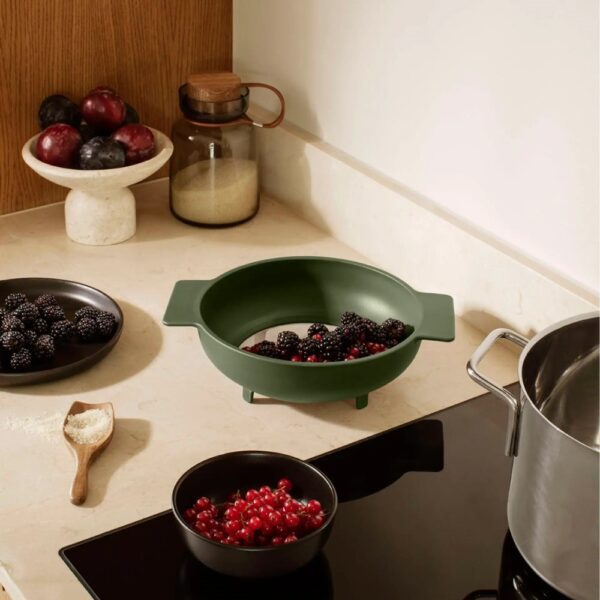 a kitchen counter with utensils and a fine mesh strainer drying berries.