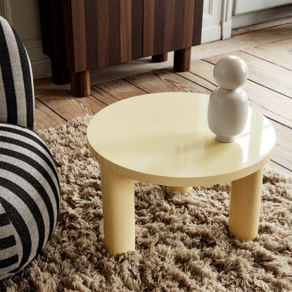 Round coffee table with cylindrical legs in living room is made from certified wood.