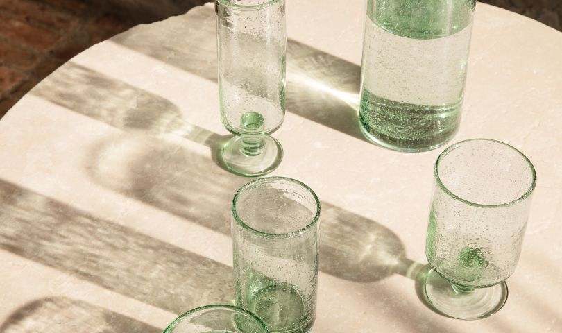 ferm LIVING's sustainable Oli range of glassware on a table with light shining through each piece.