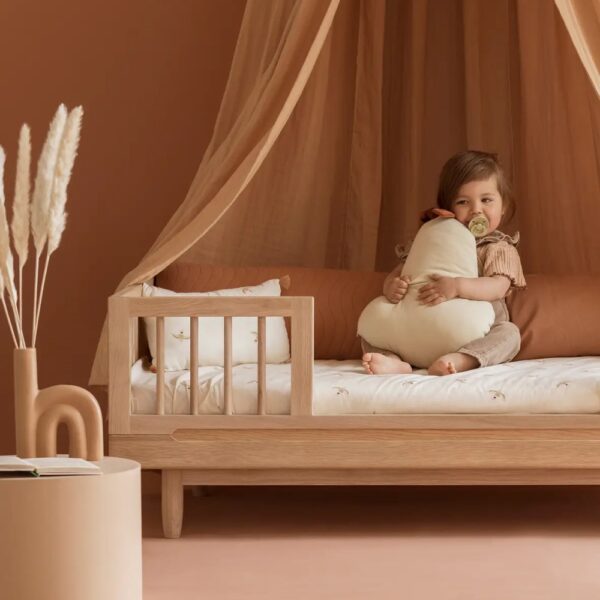 Studio lighting, perspective view of a child in a bedroom on a wooden bed frame with a security bumper installed.