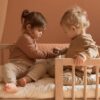 Studio lighting, perspective view of two kids playing with toys on a wooden bed frame with a security bumper installed.