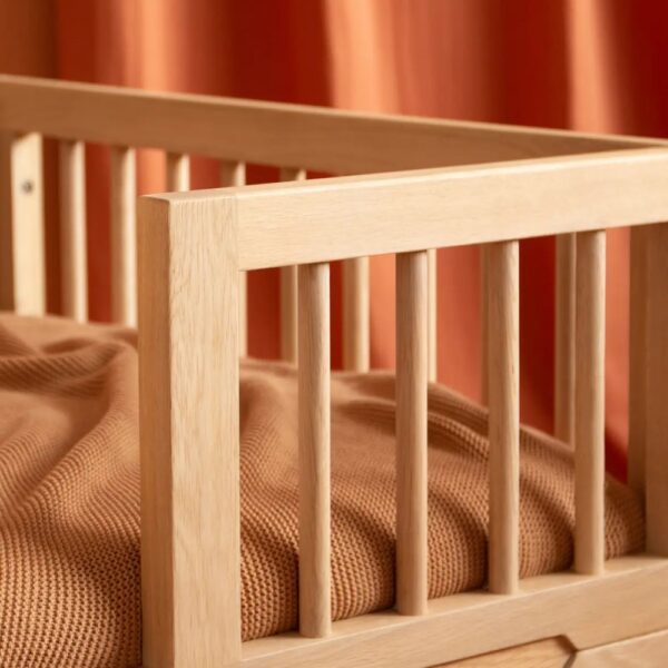 Studio lighting, detailed perspective view of a kids' wooden bed frame with a security bumper installed.