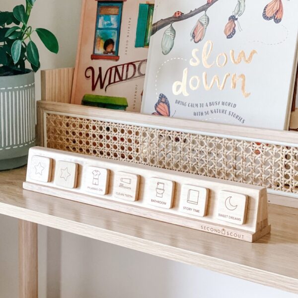 Natural lighting, perspective view of a kids' magnetic wooden stand containing magnetic, printed wooden tiles on top of a table next to a wooden book display box.