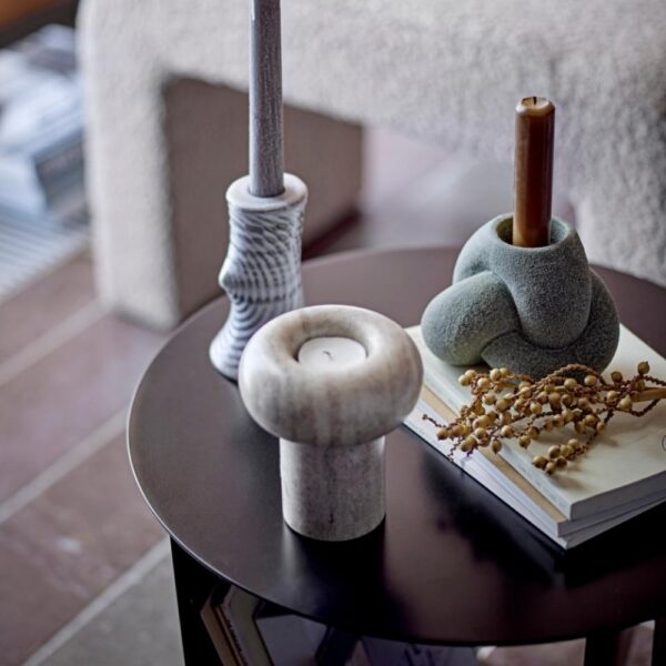Natural lighting, perspective view of a decorative candle holder on top of a table next to other abstract shaped candle holders and books.