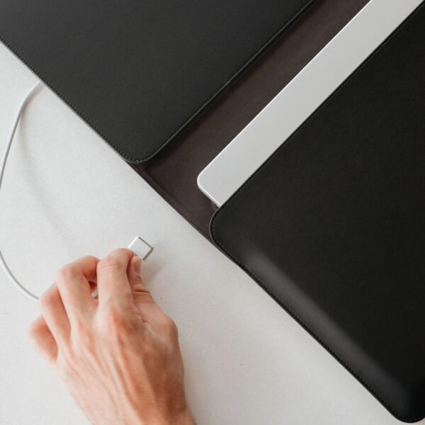 Close up of a person's hand attaching a laptop charger wire on a laptop sleeve's exposed side opening.