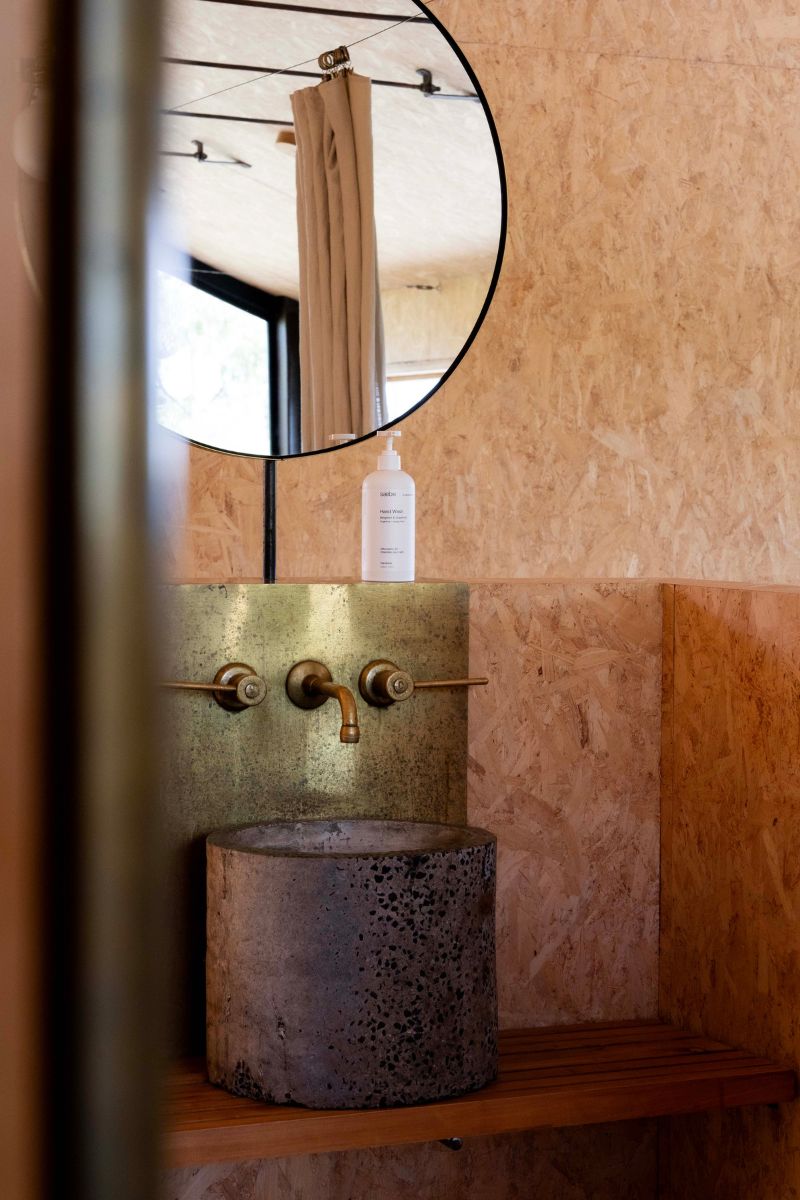 Bottle of saebe by DESIGNSTUFF hand wash on a brass and stone sink with a large round mirror above it.